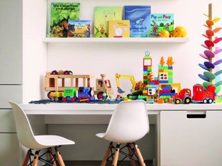 Kinderschreibtisch mit vielen Spielsachen, zwei kleinen Stühlen und einer Bücherleiste mit Büchern