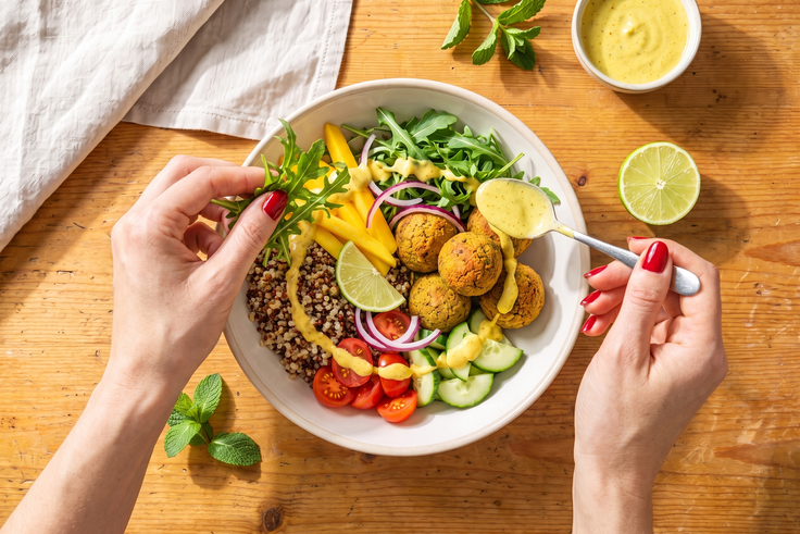 Quinoa, Gurke, Cherrytomaten, Zwiebel, Rucola, Mangostreifen und Falafel werden für Schritt 4 der Mango Falafel Bowl mit Dressing angerichtet.