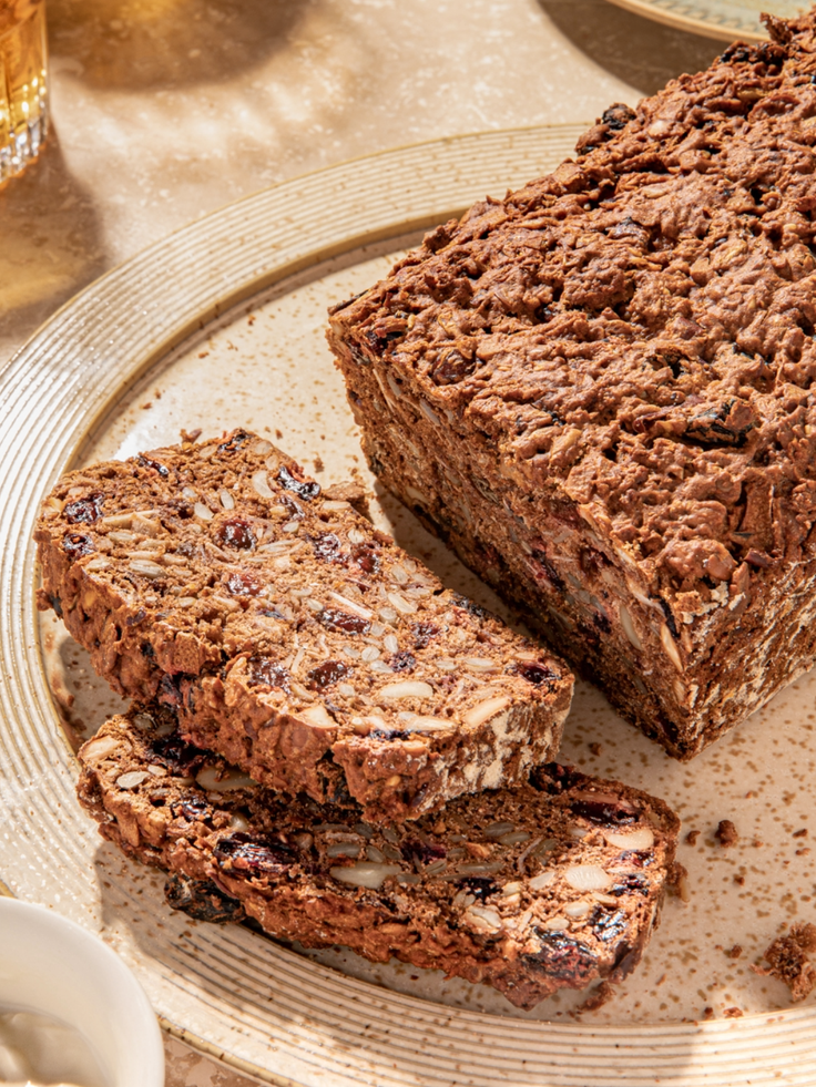 Angeschnittenes Früchtebrot mit Nüssen, Kernen und Trockenfrüchten auf einem Teller.