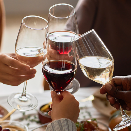 Vier Personen stoßen an einem gedeckten Tisch mit Gläsern Rotwein und Weißwein an.