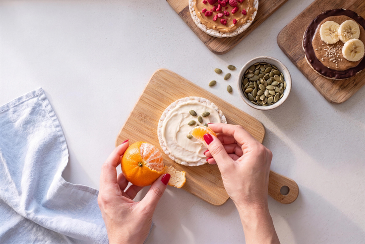 Mandarinenstücke und Kürbiskerne werden als Topping auf eine Reiswaffel mit Skyr gelegt.