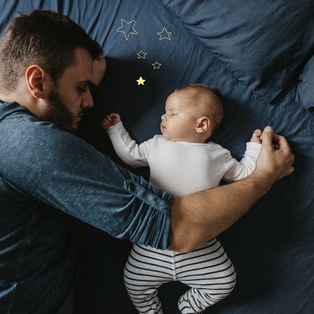 Vater schläft neben seinem schlafenden Baby, das auf blauem Stoff liegt und von goldenen Sternen umgeben ist.