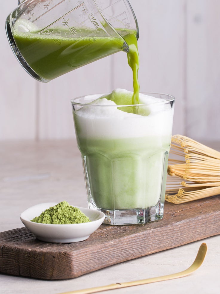 Ein Glas mit Matcha Latte auf einem Holzbrett.