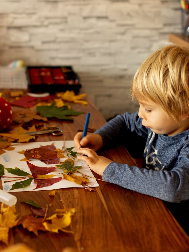 Ein Kind sitzt am Tisch und bastelt mit herbstlichen Blättern.