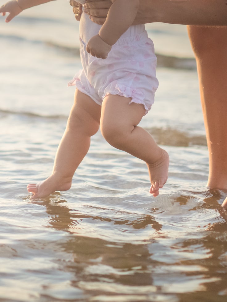 Erwachsene Person hält ein Baby beim Planschen im flachen Meerwasser während eines Urlaubs mit Baby