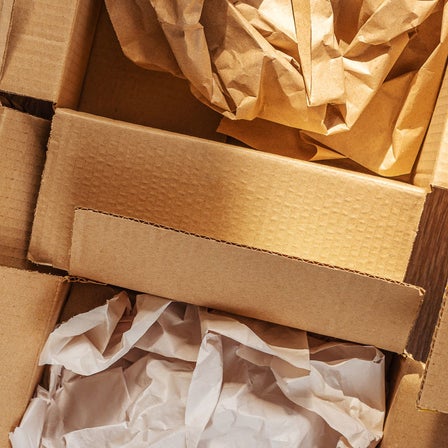 Mehrere geöffnete Kartons mit zerknülltem Packpapier in Braun, Weiß und Mintgrün.