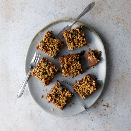 Protein Bohnenbrownies in Quadraten mit knusprigem Granola-Topping auf einem Teller auf grauem Hintergrund angerichtet.