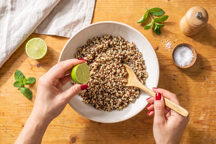 Gegarter Quinoa wird für Schritt 1 der Mango Falafel Bowl mit Limettensaft, Salz und Pfeffer in einer Schüssel abgeschmeckt.