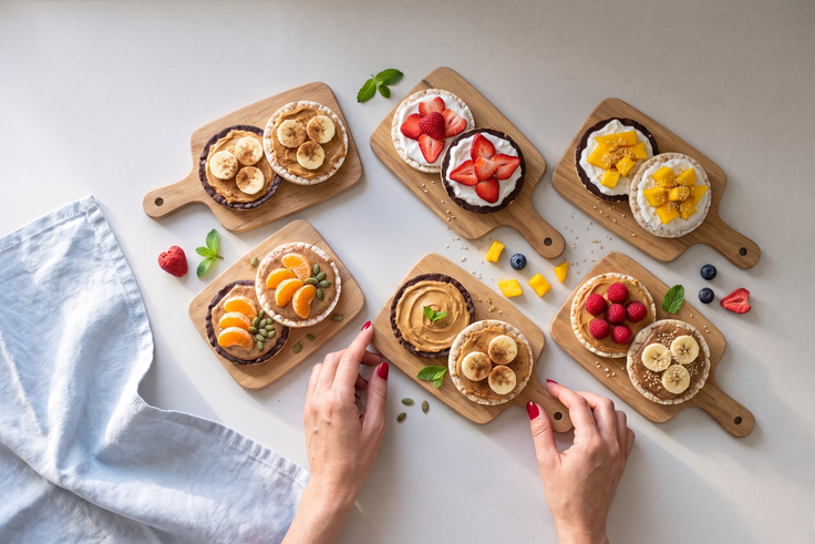 Fertig belegte Reiswaffel Variationen mit Banane, Erdbeeren, Himbeeren, Mandarine, Mango, Nussmus, Joghurt und Schokolade liegen auf Holzbrettchen.